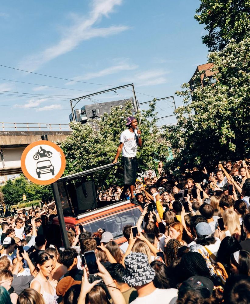 A performer standing on the roof of the red G-Class above a street crowd