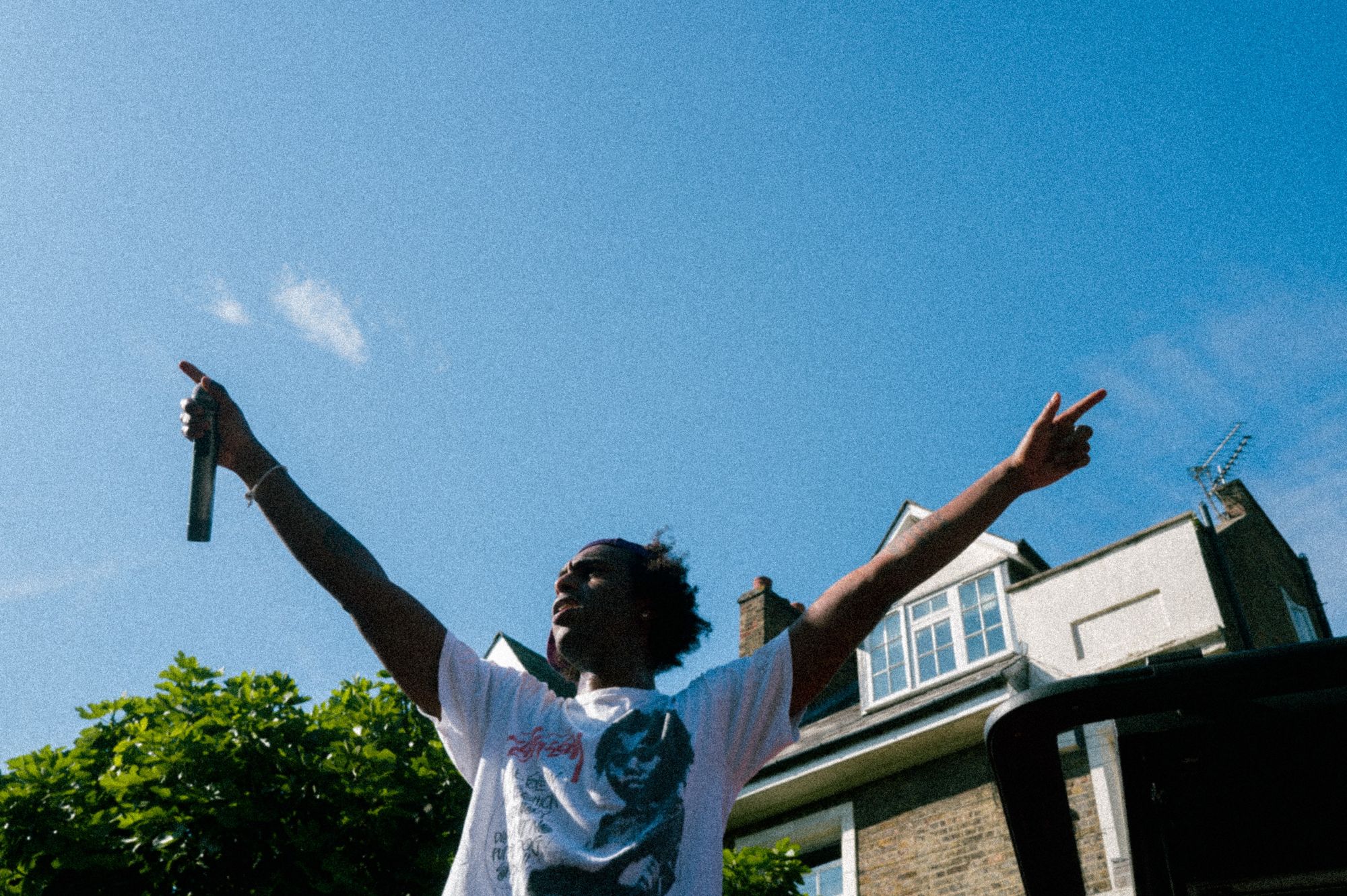 A performer with arms outstretched against a blue sky above a residential street