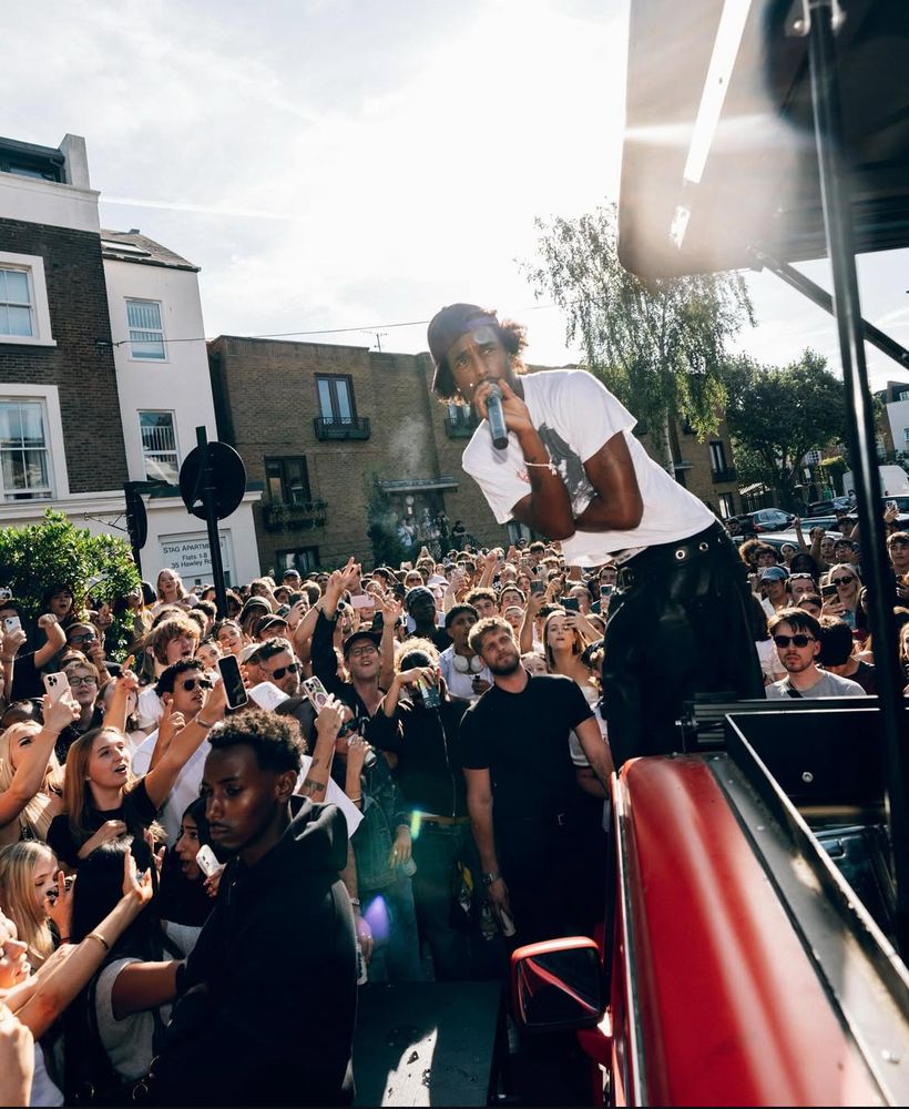 A performer leaning from the G-Class towards a dense street crowd in afternoon sun