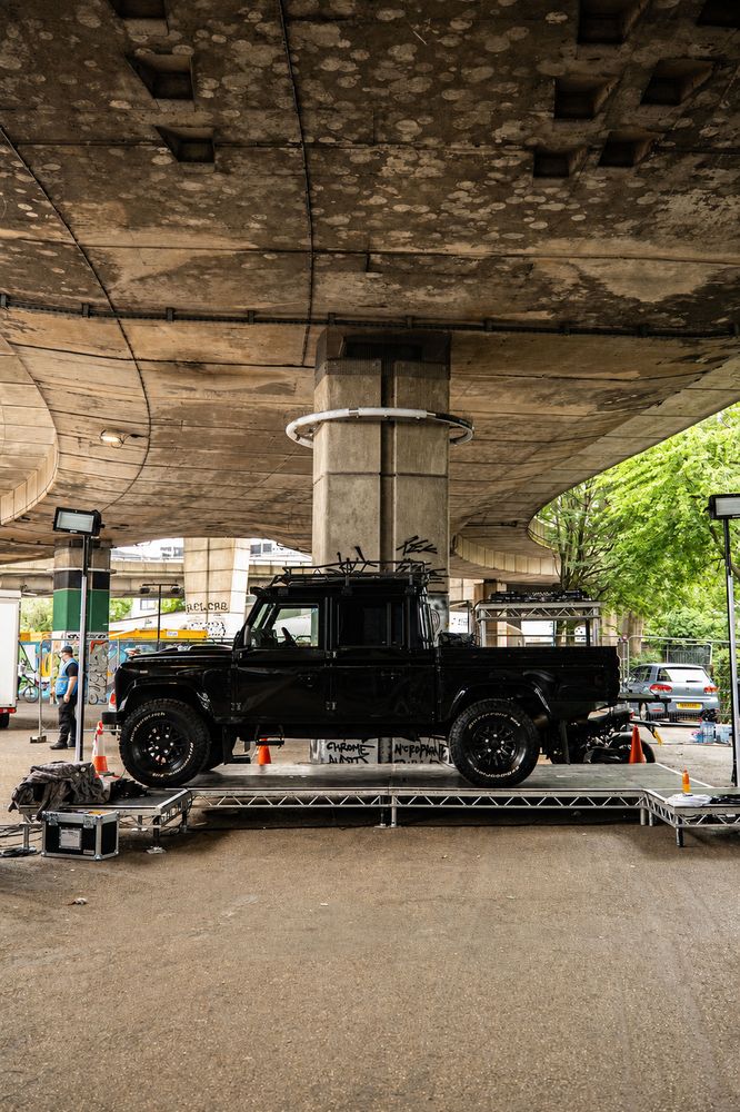 A black Land Rover Defender on a stage deck beneath the flyover before doors