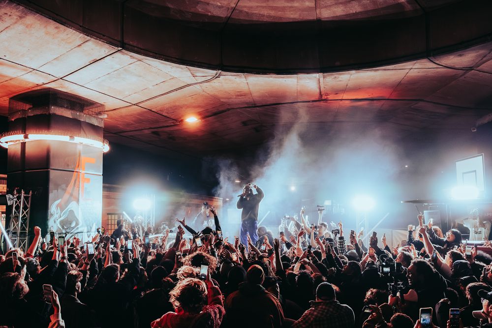 A crowd with phones raised in front of a performer under the Westway flyover at night