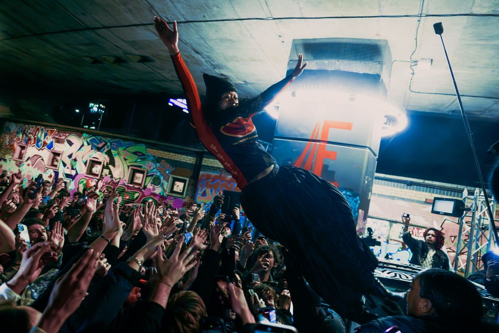 A performer dives into the crowd in front of graffiti walls under the Westway